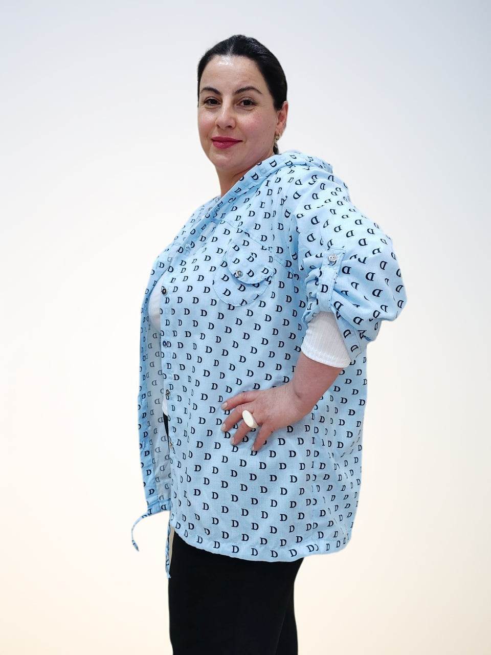 Блузка - ბამბის ბლუზა თავსახურით, side view of the light blue shirt with D letter pattern, model posing confidently.