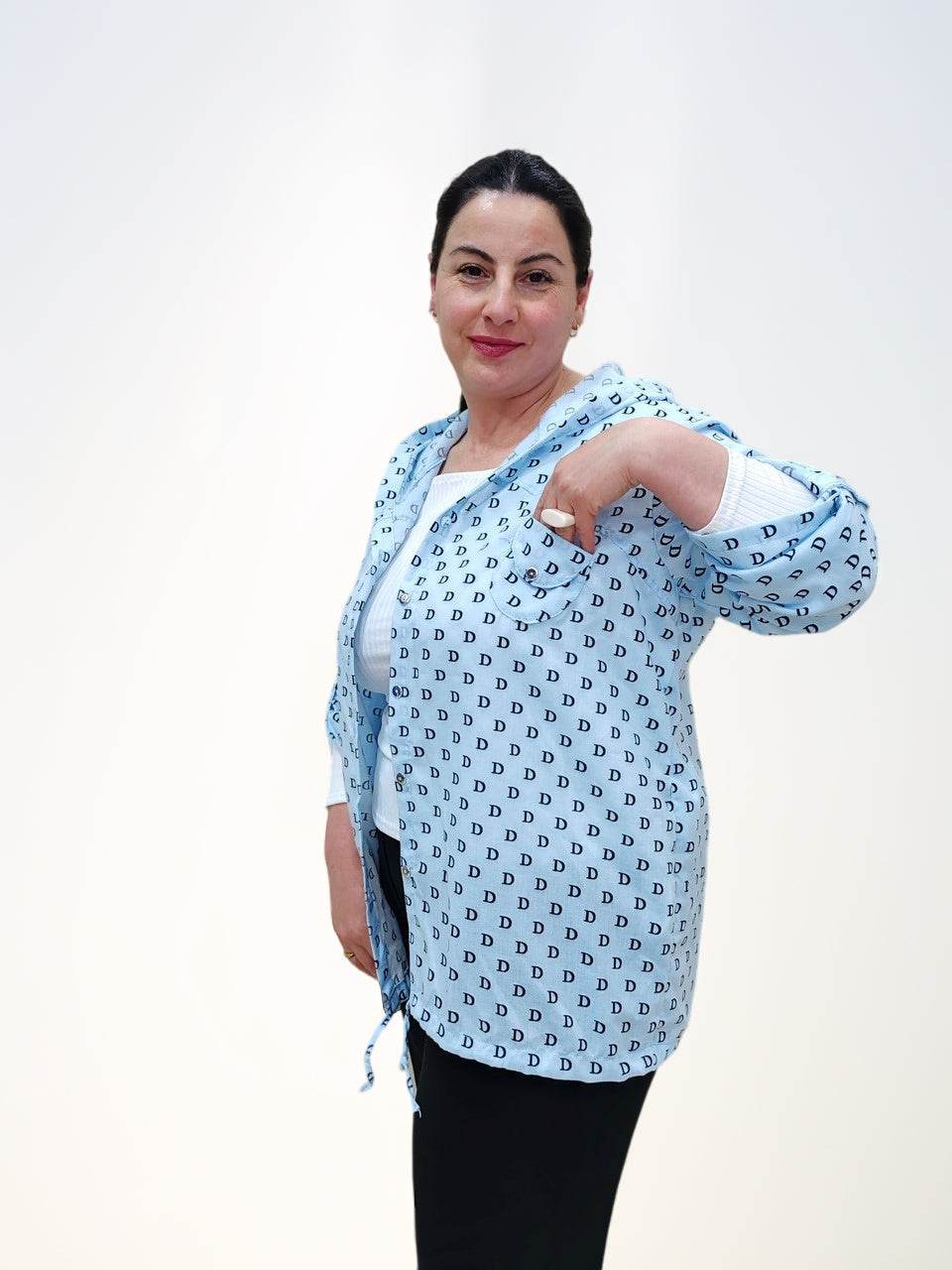 Блузка - ბამბის ბლუზა თავსახურით, model pointing at the pocket of a light blue shirt with D letter pattern.