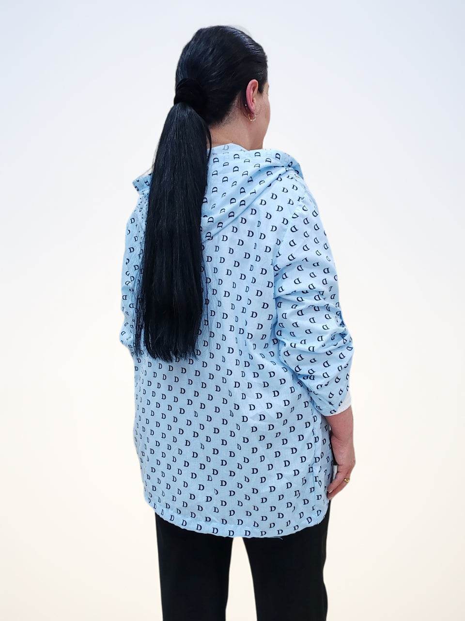 Блузка - ბამბის ბლუზა თავსახურით, showcasing back view of a light blue shirt with D letter pattern, model with long hair.
